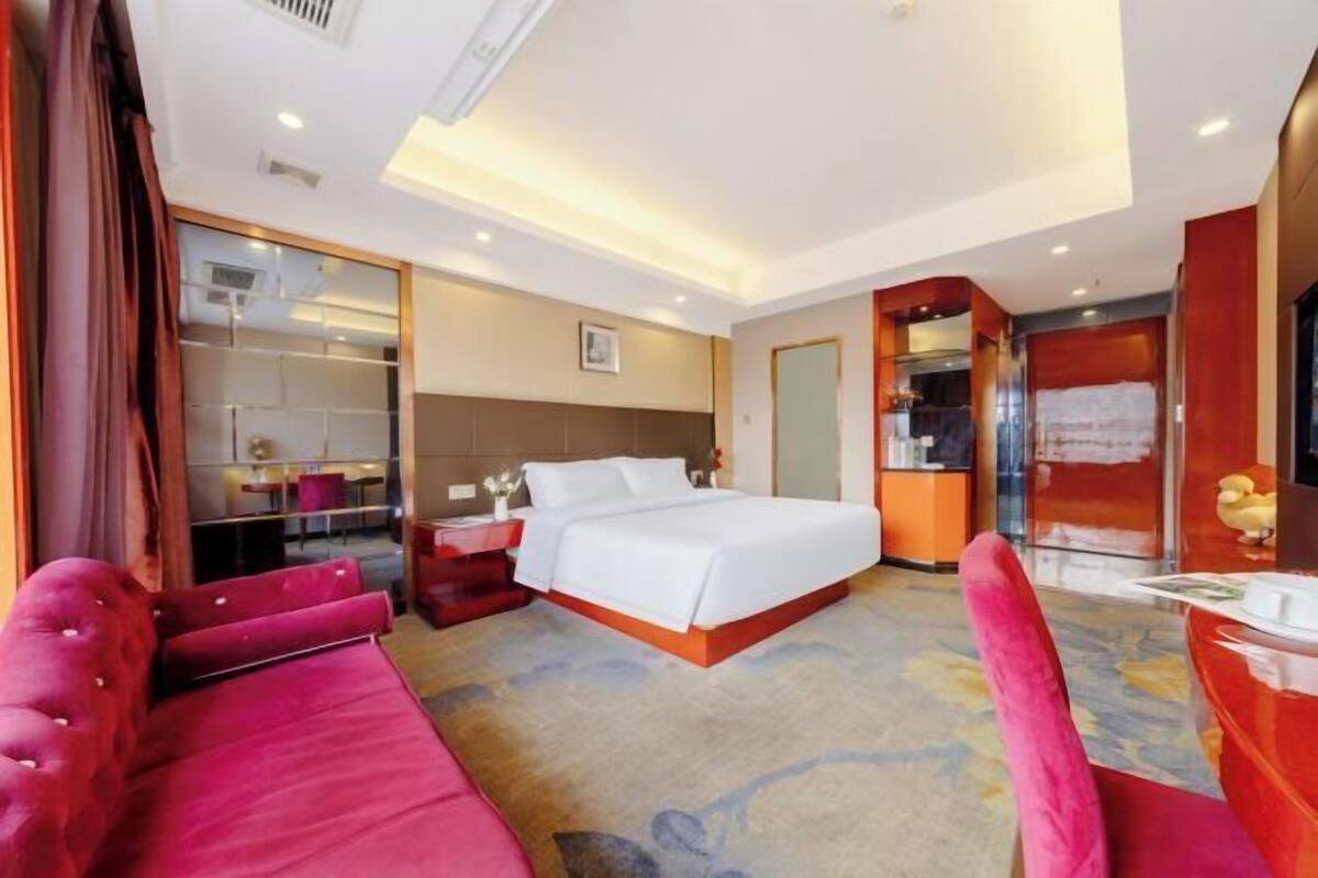 A hotel room with a large bed, a red sofa, a desk, and a mirror.