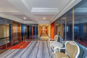 A hotel corridor with a carpeted floor, mirrored walls, and a red carpet runner. There are chairs and a small table along the corridor. - Xinyue Theme Hotel (Longjiang Convention and Exhibition Center Shop) (Foshan)