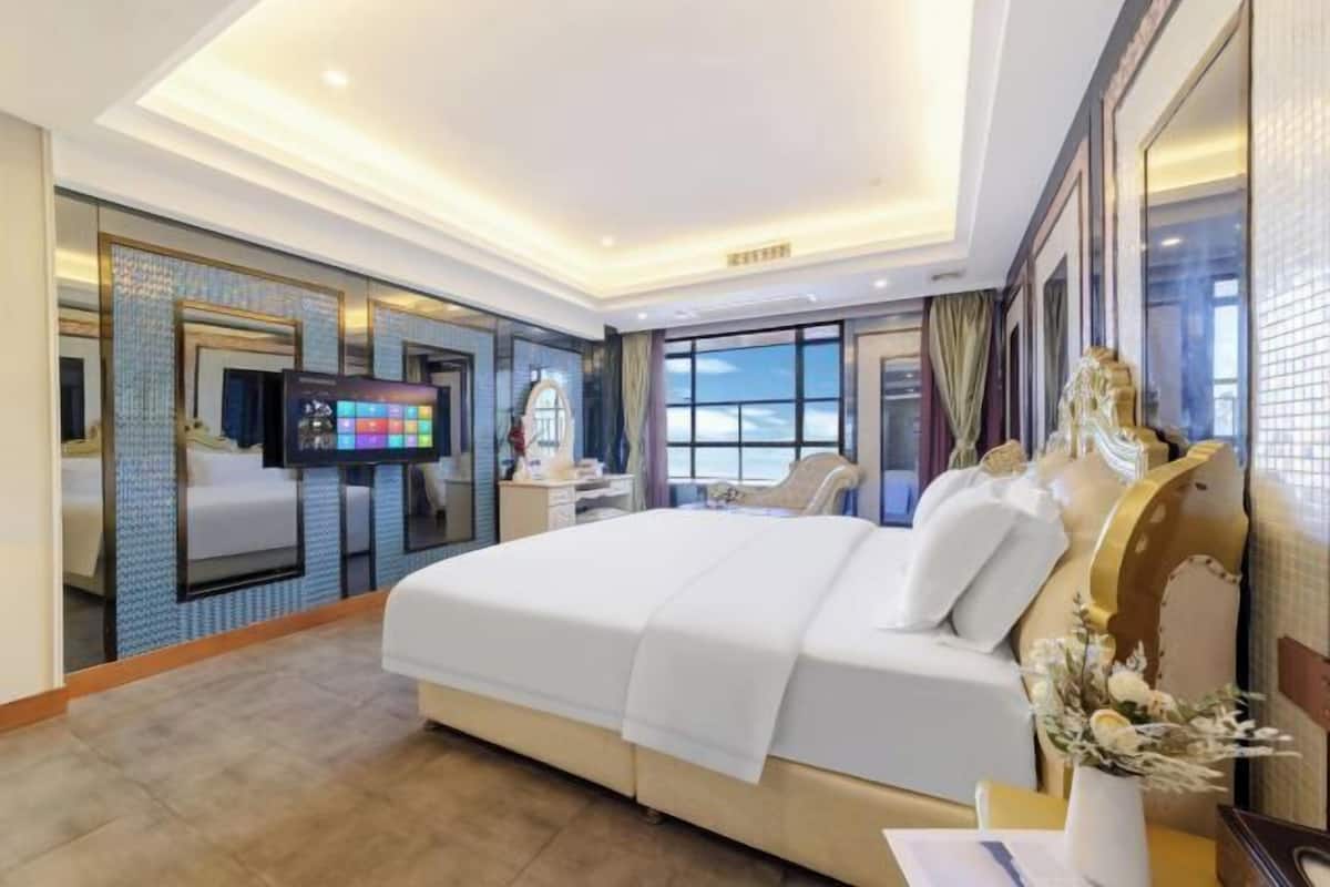 A hotel room with a large bed, a desk, a television, and a view of the sea.