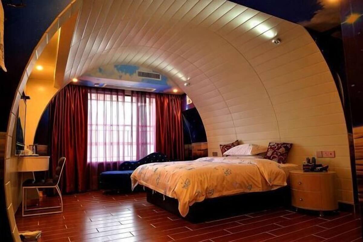 A bedroom with a curved ceiling, a bed, a desk, and a chair.