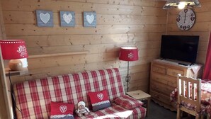 A cozy room with a plaid sofa, two red lamps, a wooden dresser, and a television. - Wifi, Ground floor, parking, tv, ski locker, 15m², Les Gets (Les Gets)