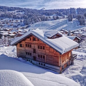A wooden chalet with a balcony, surrounded by snow-covered trees and a ski slope in the background. - Wifi, 350m from ski lifts, 2nd floor, balcony, parking, tv, ski locker, 62m², Les Gets (Les Gets)