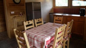 Cocina de una cabaña de madera con una mesa, sillas, un refrigerador, un reloj y una ventana.