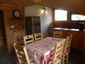 Une cuisine rustique aménagée dans une cabane en bois, avec une table et des chaises, un réfrigérateur, une horloge et une fenêtre.