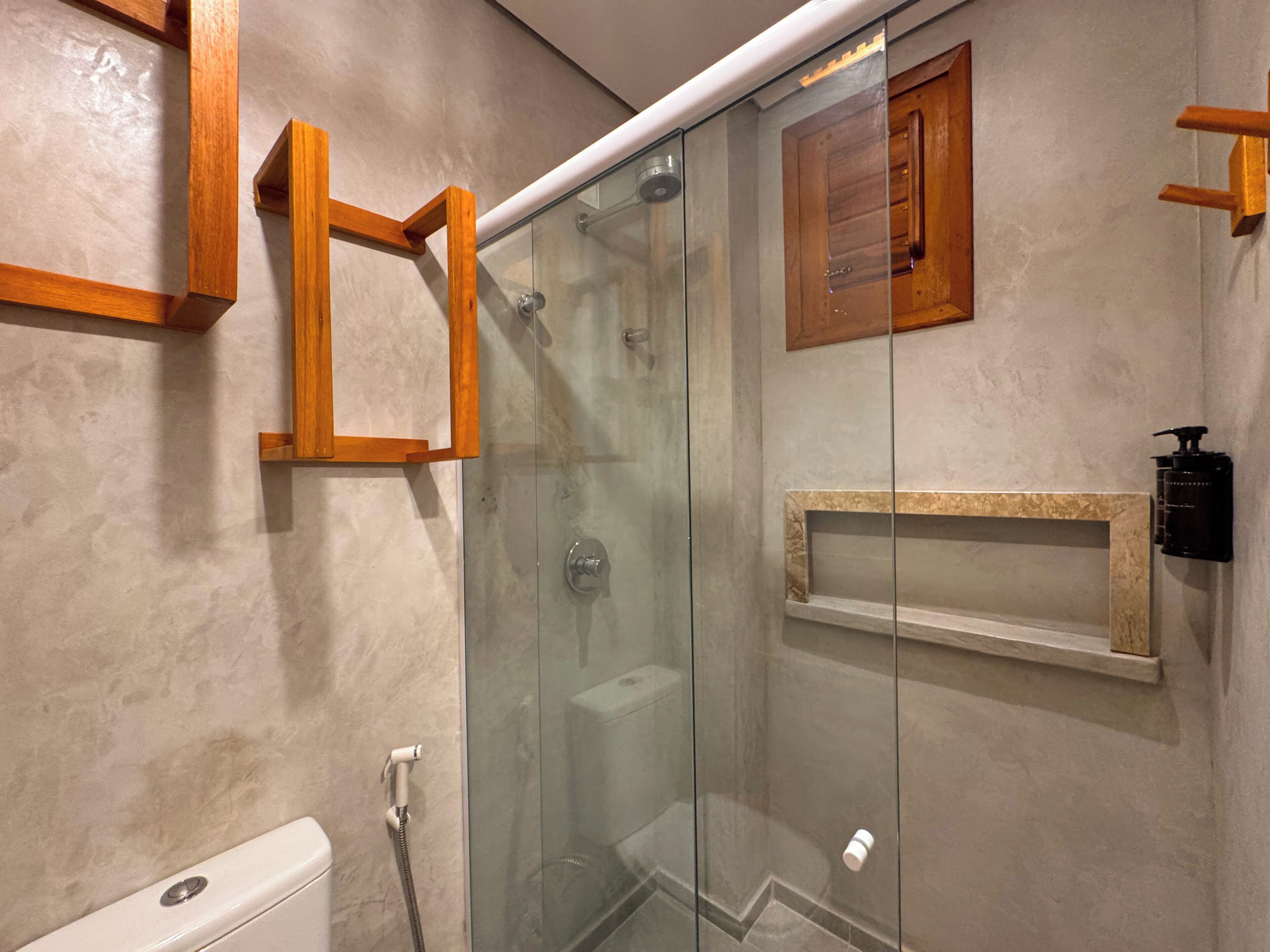 A modern bathroom with a glass-enclosed shower, a wooden shelf, and a marble countertop.