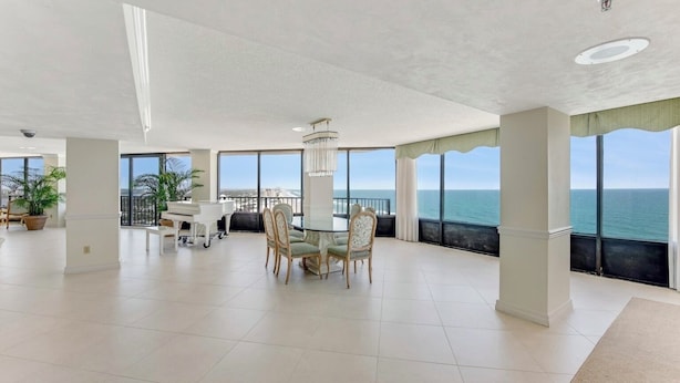 A spacious room with a large dining table, chairs, and a view of the ocean through large windows.