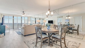 A spacious living area with a large sofa, a dining table with chairs, and a ceiling fan.