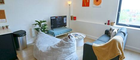 A modern living room with a sofa, a bean bag, a TV, and a window with a view.