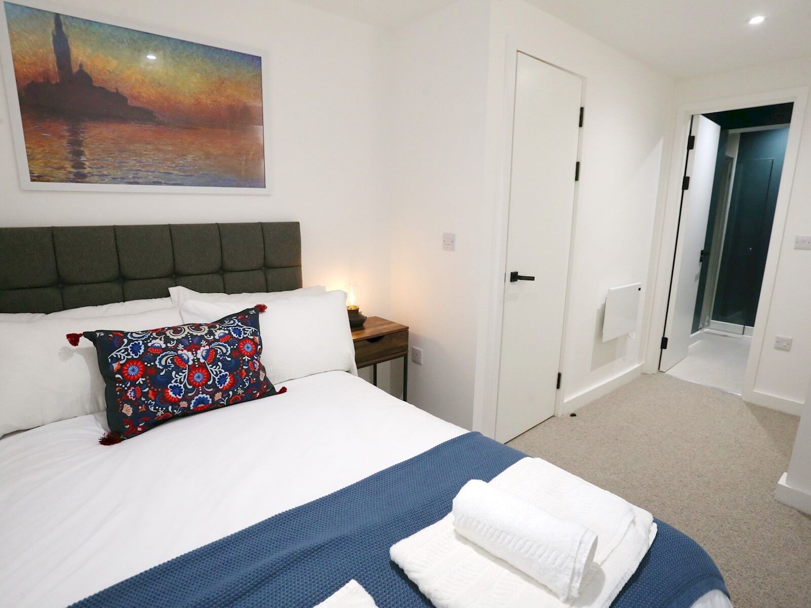 Une chambre d’hôtel avec un lit, une table de chevet, un tableau et une porte donnant sur une autre pièce.
