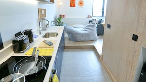 A compact kitchen with a stove, sink, and modern appliances. There is a dining area with a couch and a plant. - Central Trafford Duplex With Shop at Base - Pass the Keys (Manchester)