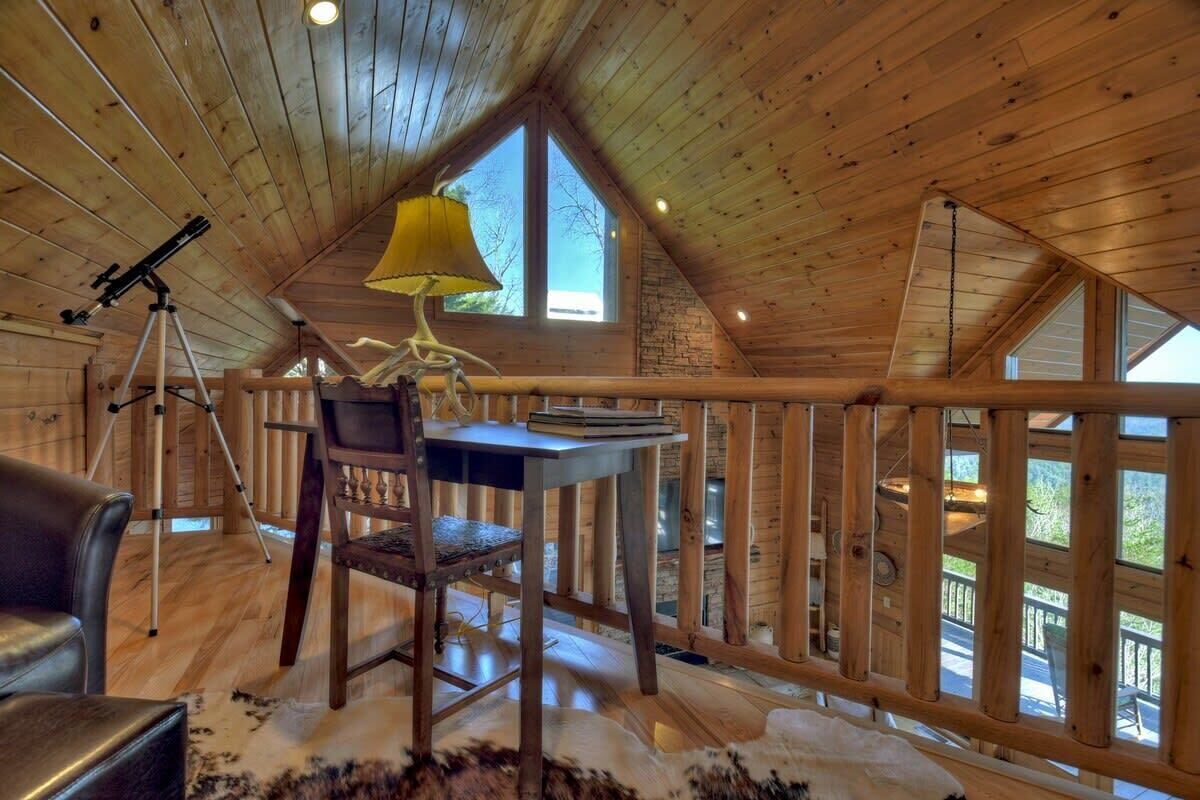 A cozy cabin with a wooden interior, a telescope, a desk with a lamp, and a view of the outdoors.