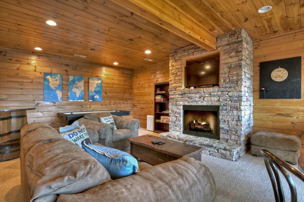Ein gemütliches Blockhaus-Interieur mit Kamin aus Stein, Ledersofas und einer Weltkarte an der Wand.