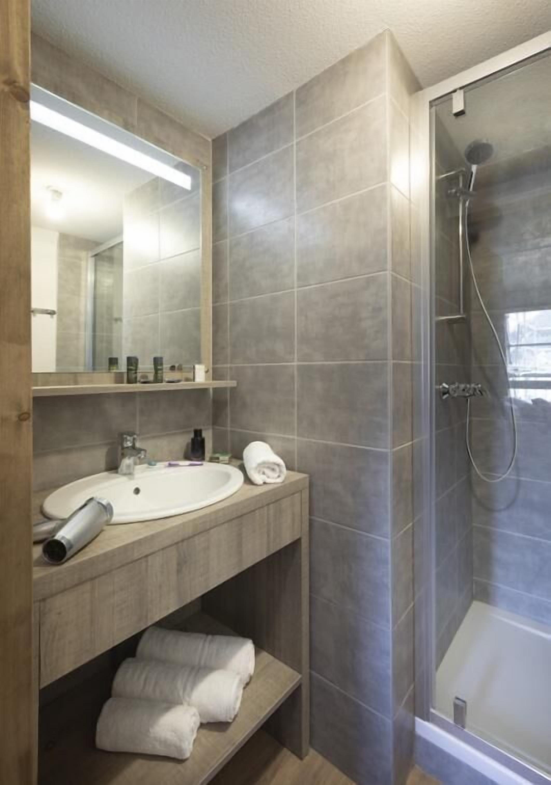 Ein modernes Badezimmer mit großem Spiegel, Waschbecken, Dusche und Handtuchhalter.
