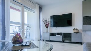 Uma sala de estar moderna com uma mesa de vidro, uma TV fixada na parede e uma varanda com uma cadeira.