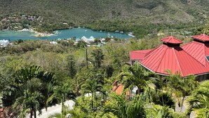 Blick auf die Küste mit einem Gebäude mit rotem Dach, üppiger Vegetation und einem Hafen mit Booten.