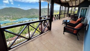 Ein Balkon mit Blick auf einen See und Berge, möbliert mit Korbstühlen und einem Tisch.