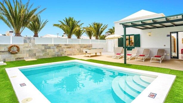 A swimming pool with a sun terrace, lounge chairs, and palm trees. - Villa Atlantico Mar by Villa Plus (Tías)