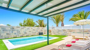 A modern outdoor pool area with a stone wall, artificial grass, and lounge chairs with towels. - Villa Atlantico Mar by Villa Plus (Tías)