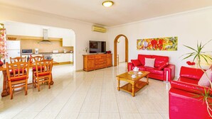 A living room with a red sofa, wooden coffee table, and a TV. There is a kitchen area with white cabinets and a microwave. - Villa Atlantico Mar by Villa Plus (Tías)