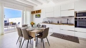A modern kitchen with white cabinetry, a wooden countertop, and built-in appliances. There is a dining area with a table and chairs, and a view of the outdoors. - Villa Andromeda by Villa Plus (Santa Maria del Focallo)