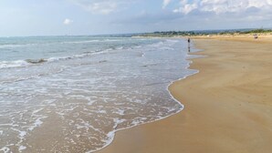 A wide sandy beach with gentle waves, a clear sky, and a distant cityscape. - Villa Ares by Villa Plus (Santa Maria del Focallo)