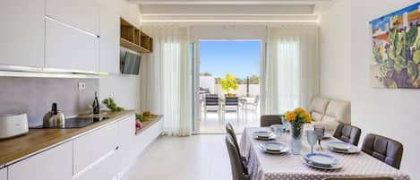 A modern kitchen with a dining area, a view of the outdoors, and a cactus painting on the wall.