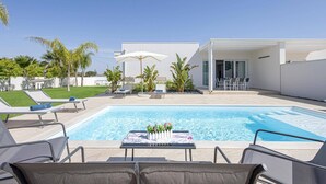A modern pool area with lounge chairs, a table with flowers, and a building with a patio. - Villa Ares by Villa Plus (Santa Maria del Focallo)
