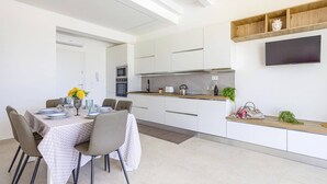 A modern kitchen with white cabinetry, a built-in oven, microwave, and a wooden shelf above the counter. - Villa Ares by Villa Plus (Santa Maria del Focallo)