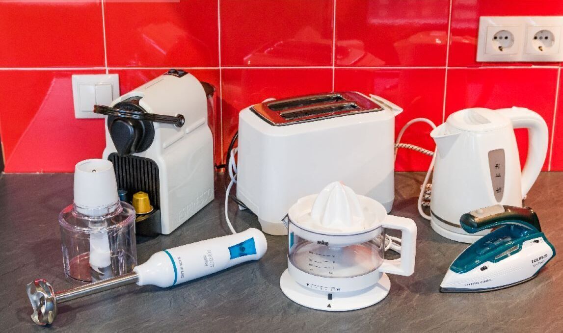 A kitchen counter with a toaster, a kettle, a juicer, an iron, and a bottle of hand soap.