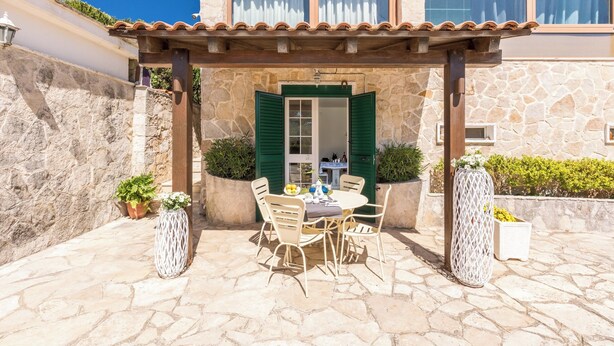 A stone building with a tiled roof, a balcony, and a table with chairs.