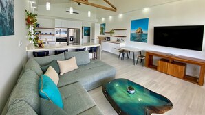 A modern living room with a grey sectional sofa, a coffee table, a TV, and a kitchen area in the background. - Flamingo Marina Penthouse Condo (Playa Flamingo)