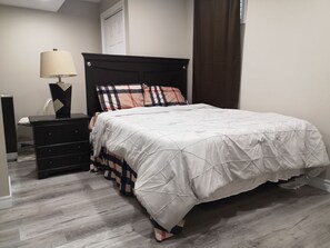 A bedroom with a bed, a dresser, a lamp, and a window with curtains. - Comfortable 2-bedroom walk out basement (Hagersville)