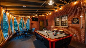 Ein Billardraum mit Pooltisch, Stühlen, Dartscheibe und Fernseher.