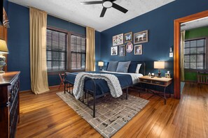 A bedroom with a bed, bedside tables, a desk, a ceiling fan, and a window with blinds.
