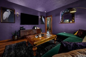 A room with a flat-screen TV, a wooden coffee table, a green sofa, and a mirror with a decorative frame.