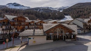 Un conjunto de edificios de madera con balcones, probablemente un hotel o resort, con el paisaje de montañas nevadas y un valle boscoso al fondo.