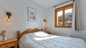 Un dormitorio con cama de madera, dos mesitas de noche con lámparas, un cuadro enmarcado con un búho y una ventana con vistas a un edificio y árboles.
