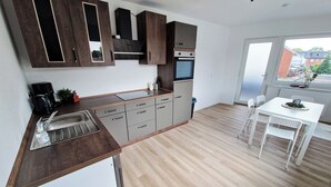 A modern kitchen with dark wooden cabinets, a built-in oven, and a white dining area with a table and chairs. - Weser Pension - Zweibettzimmer mit Eigenem Bad Nr. 1 (Brake (Unterweser))