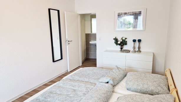 A bedroom with a bed, a dresser, a mirror, and a door leading to a bathroom. - Weser Pension - Zweibettzimmer mit Eigenem Bad Nr. 1 (Brake (Unterweser))