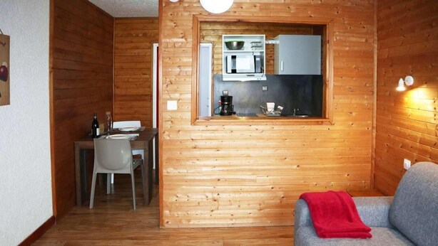 A cozy cabin interior with a wooden interior, a kitchenette with a microwave, a dining area with a table and chairs, and a grey sofa with a red blanket. - 100m from ski slopes, 1st floor, view valley, tv, ski locker, 20m², Les Orres (Les Orres)