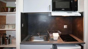 Uma cozinha compacta com micro-ondas integrado, pia e pequena geladeira.