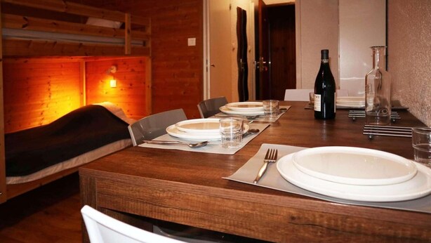 Un coin repas avec une table en bois mise pour quatre personnes, comprenant des assiettes, des couverts et des verres.