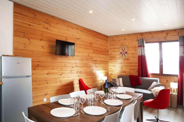 A wooden-paneled room with a dining table set for four, a sofa, and a television mounted on the wall.