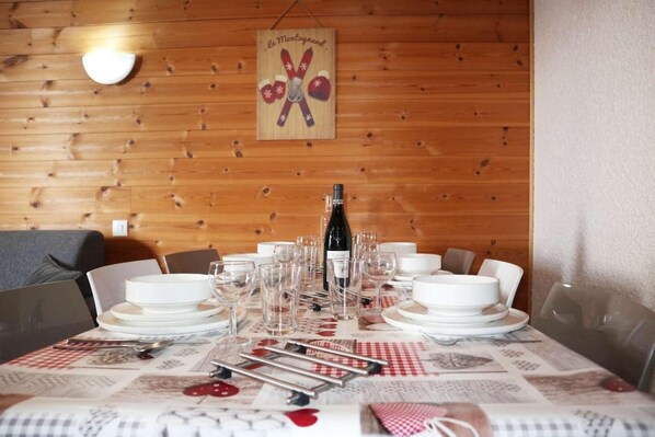 A dining table set with white plates, glasses, and cutlery, a bottle of wine, and a red and white checkered tablecloth.