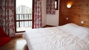 Un dormitorio con una cama grande, paredes de paneles de madera, un balcón con cortinas estampadas y una silla roja.
