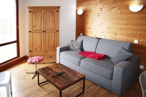 A room with a grey sofa, a wooden cabinet, a wooden coffee table, and a window.