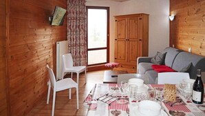 Una habitación acogedora con paredes de madera, un sofá gris, una mesa de comedor con platos y vasos blancos, y un mantel a cuadros rojo y blanco.