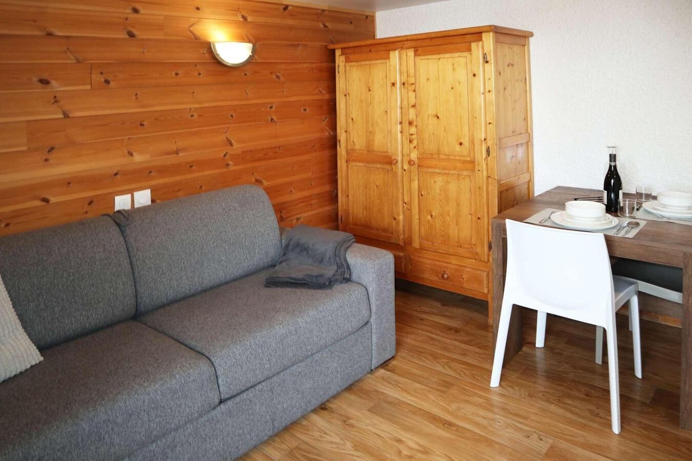 A cozy room with a grey sofa, wooden cabinets, and a dining table set for two.