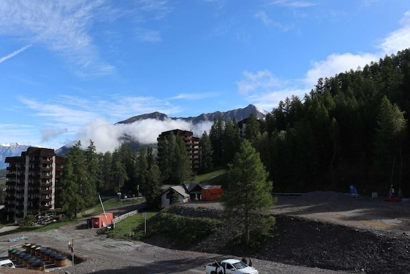 A mountainous area with a building that has multiple floors and balconies, surrounded by dense forest and a clear sky.