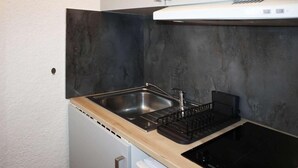 A compact kitchen with a stainless steel sink, a black dishwasher, and a black stove.